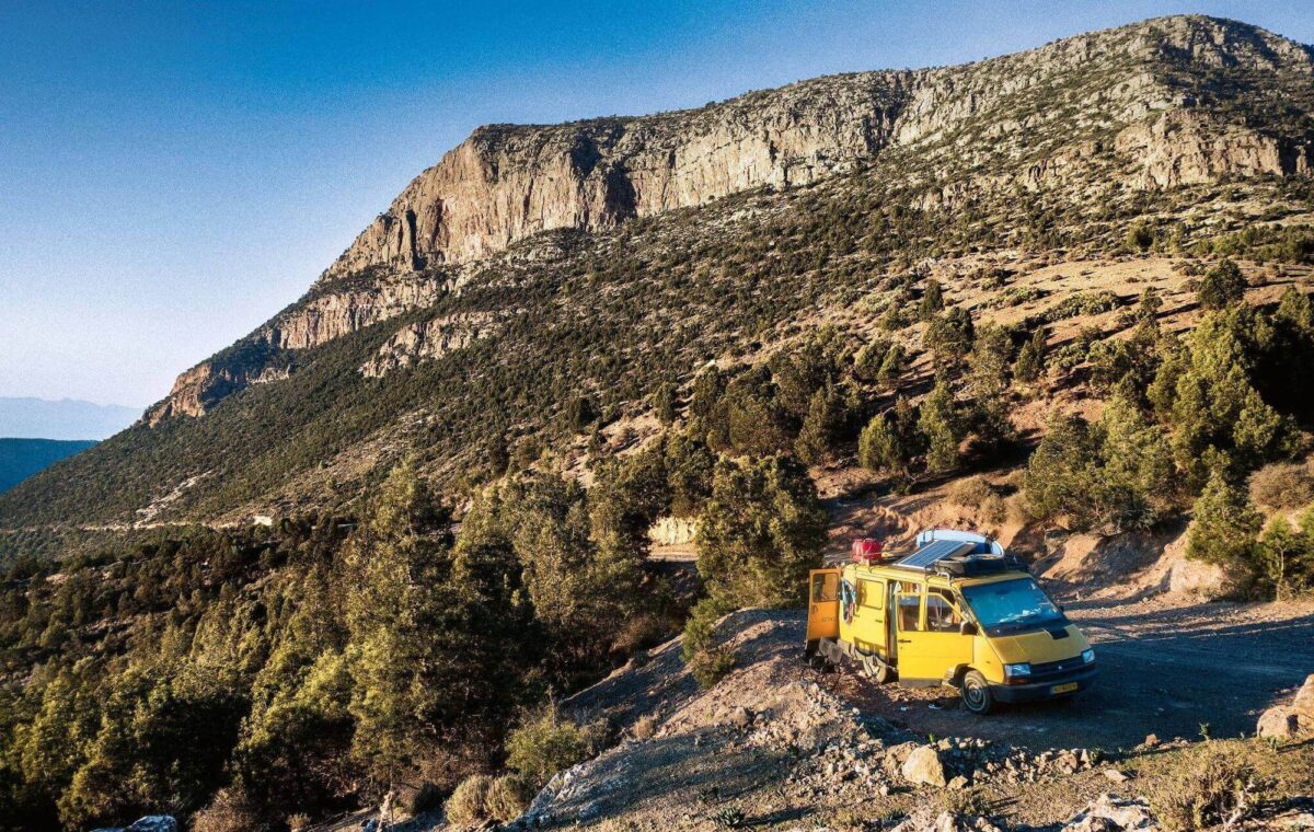 Ein gelber Campingbus mit einer installierten PV-Anlage steht in den Bergen.