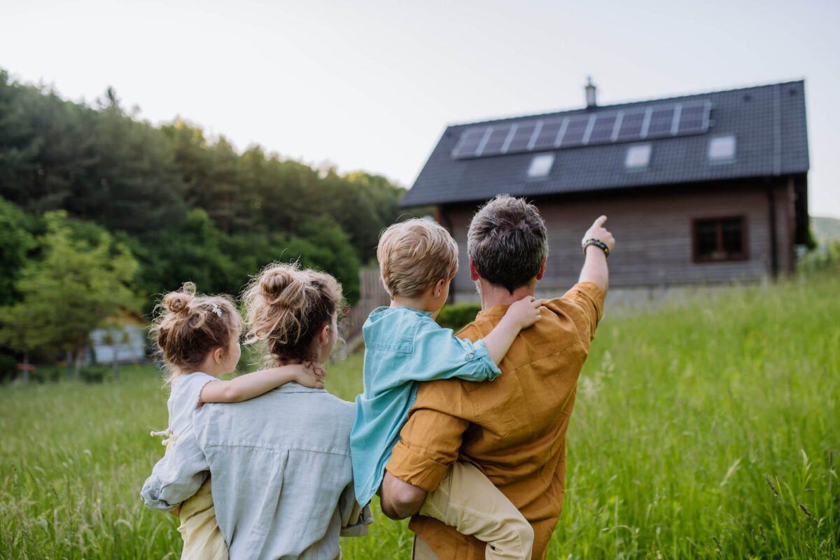 Familie zeigt auf ein Haus mit Photovoltaik-Anlagen auf dem Dach inmitten der Natur.