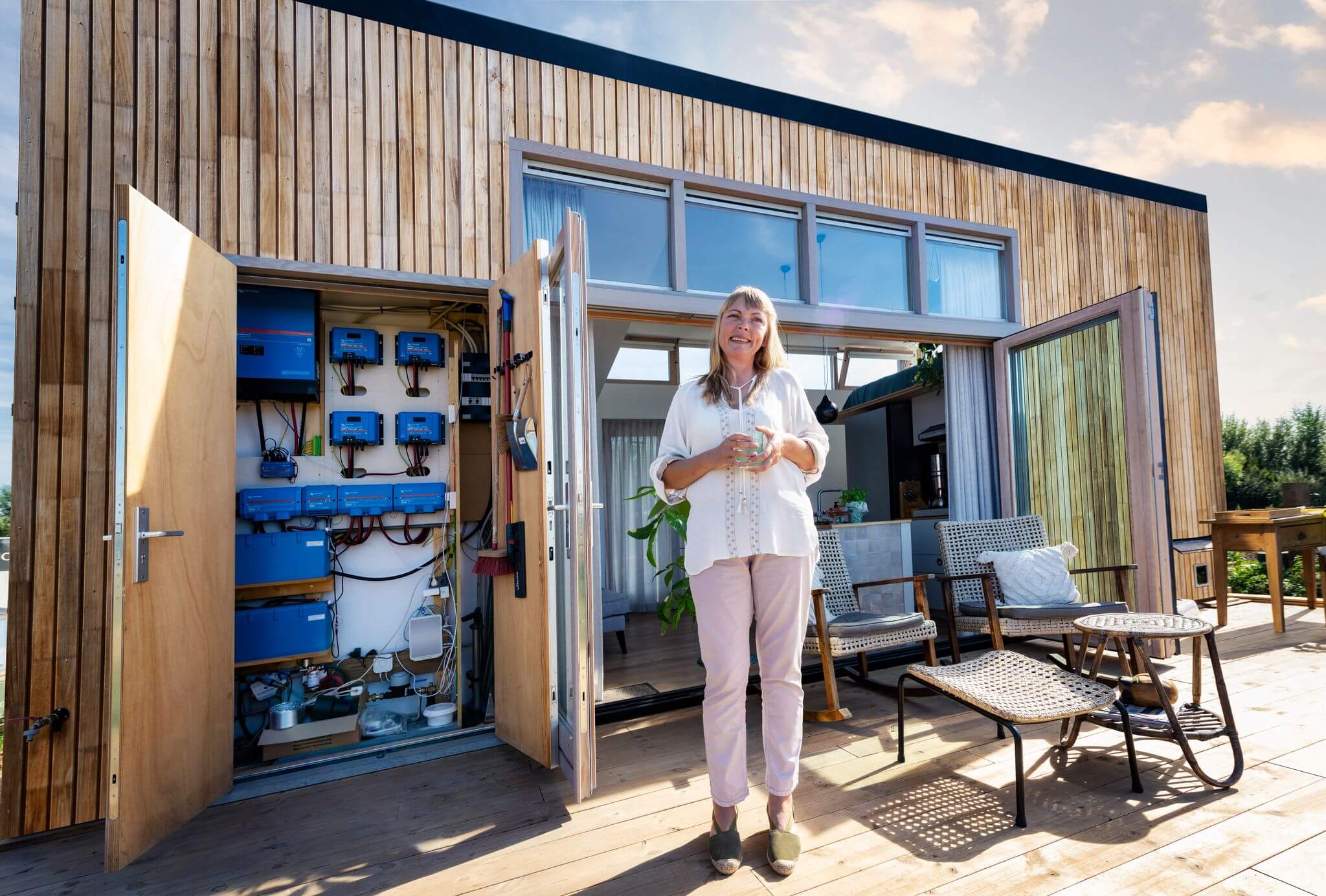 Eine Frau steht neben einem modernen Holzhaus, das mit einer Photovoltaik-Anlage ausgestattet ist.