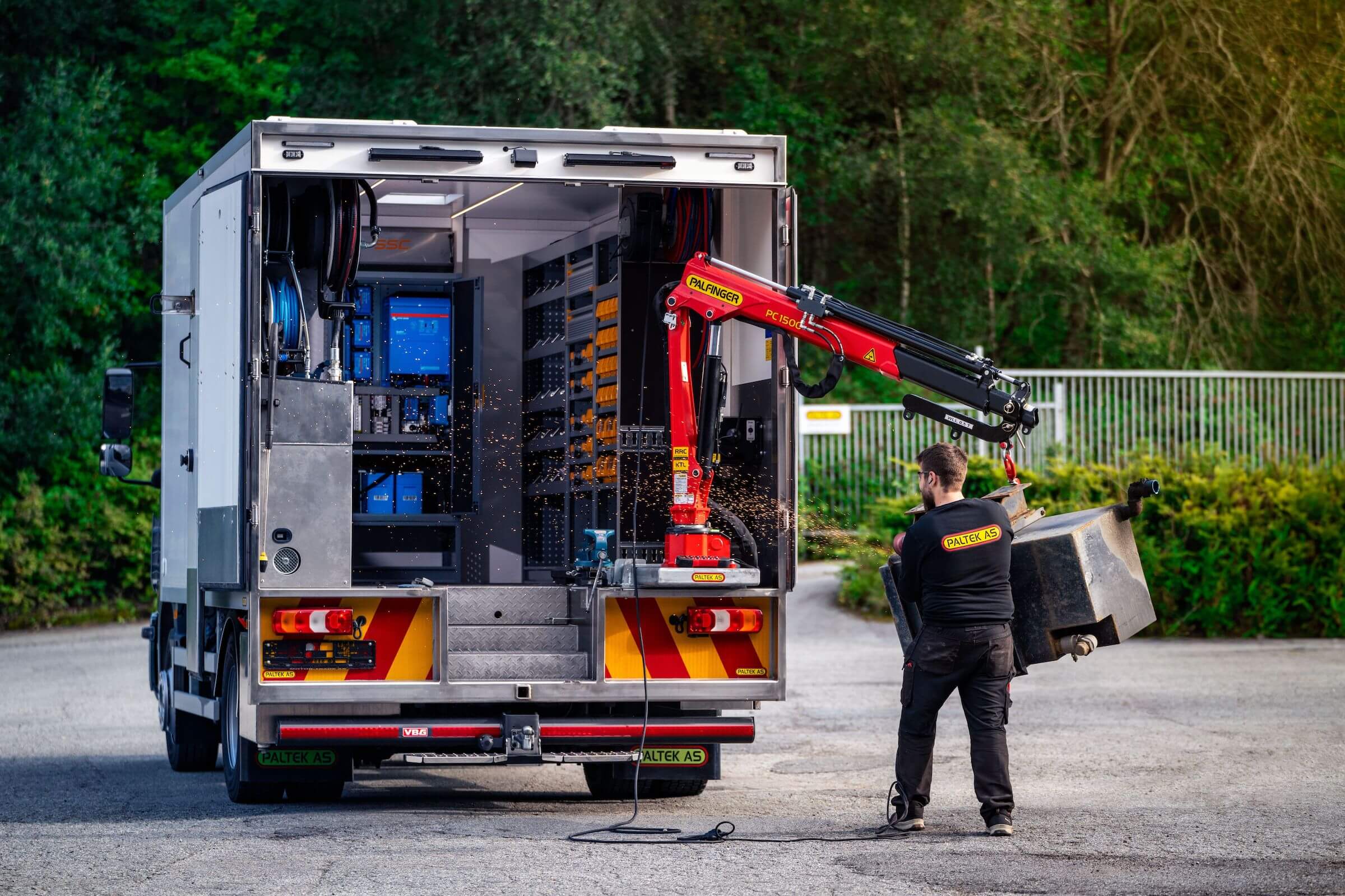 LKW mit offenem Heck, ausgestattet mit einem Kran und Hybridgeneratoren von Victron Energy, während ein Arbeiter eine schwere Last hebt.