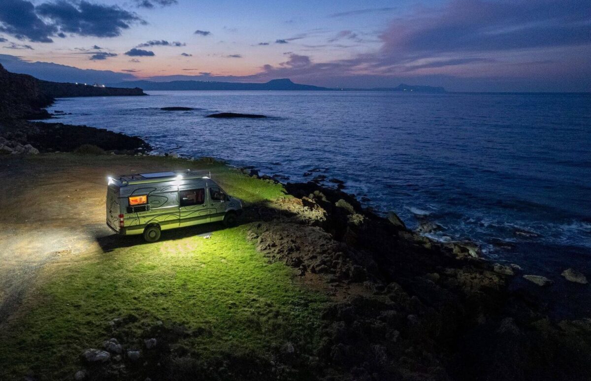 Wohnmobil steht abends mit eingeschaltetem Licht an einem Ufer, betrieben durch eine energieautarke Stromversorgung.