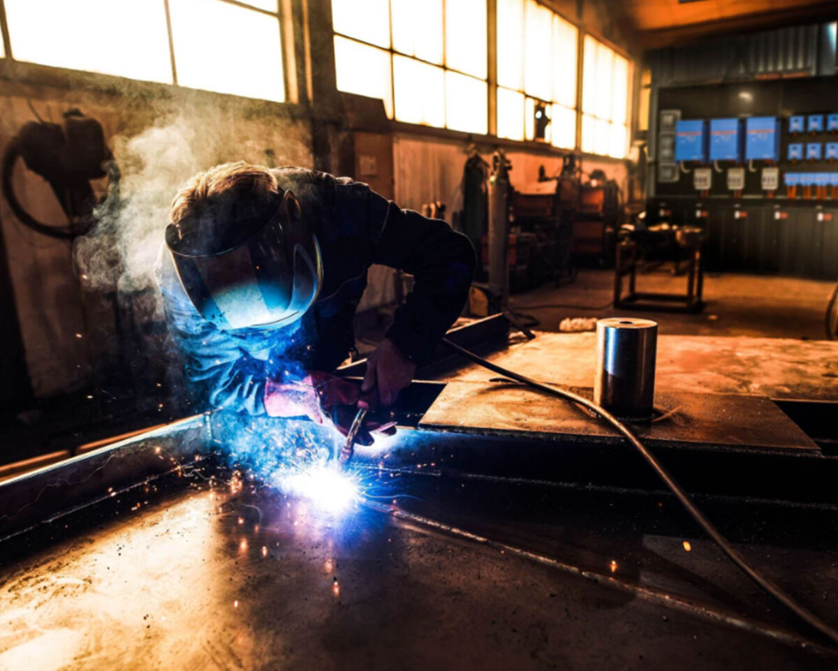 Schweißer in einer Werkstatt bei der Arbeit, Funken fliegen, während Metall bearbeitet wird.